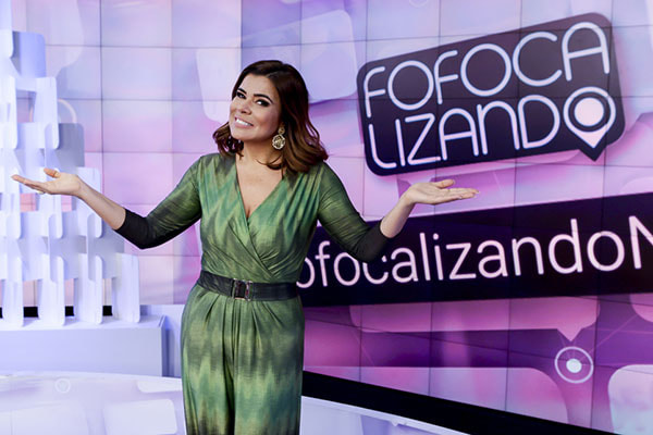 Mara Maravilha posa sorrindo de braços abertos no cenário do programa Fofocalizando