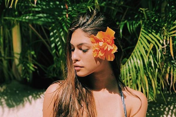 fe concon aparece olhando para o lado, na praia, com flor no cabelo