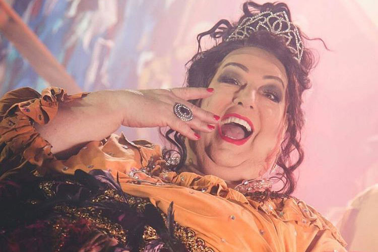 mamma aparece fantasiada, de peruca, com coroa na cabeça e sorrindo