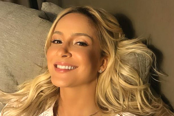 Claudia Leitte sorri para a câmera deitada na cama