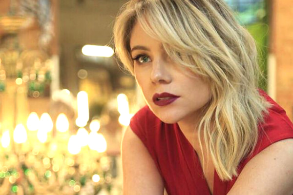 Com vestido vermelho e cara provocante, Juliana Baroni posa apoiada em mesa, com velas ao fundo