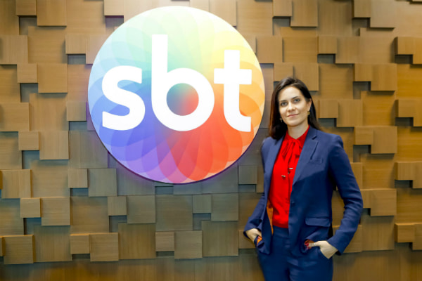 Débora Bergamasco posa ao lado do logo do SBT