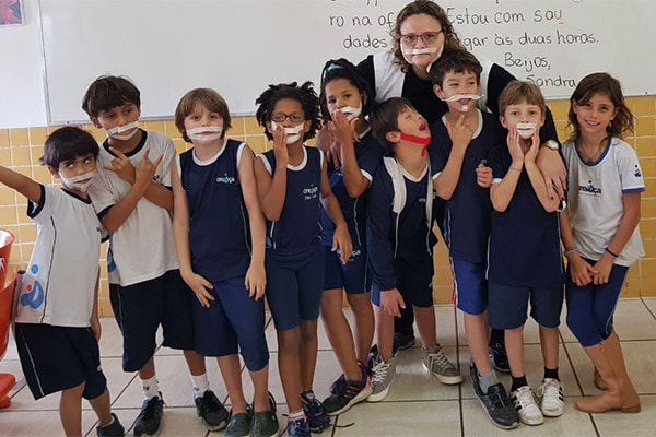 Estudantes posam para foto com fitas adesivas coladas no rosto para ajudar colega com Síndrome de Down