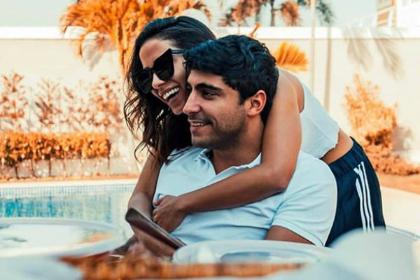 De óculos escuros, Anitta abraça seu marido, Thiago Magalhães, e dá risada