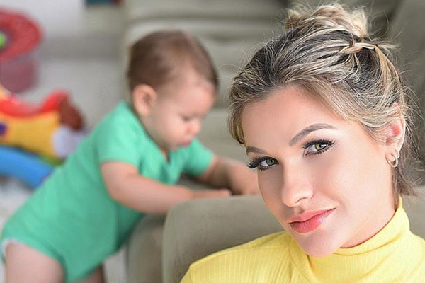 Andressa Suita aparece com blusa amarela e maquiada, com o filho Gabriel ao fundo