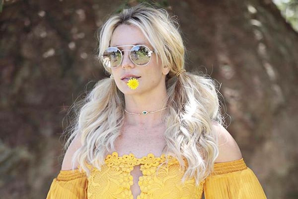 Com vestido amarelo, Britney Spears segura flor na boca