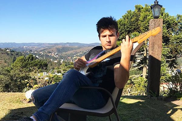 Nicholas Torres toca guitarra com paisagem paradisíaca ao fundo