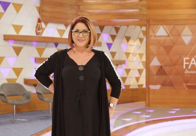 Dra. Anahy usa um vestido largo e preto, um óculos redondo, listrado preto e branco