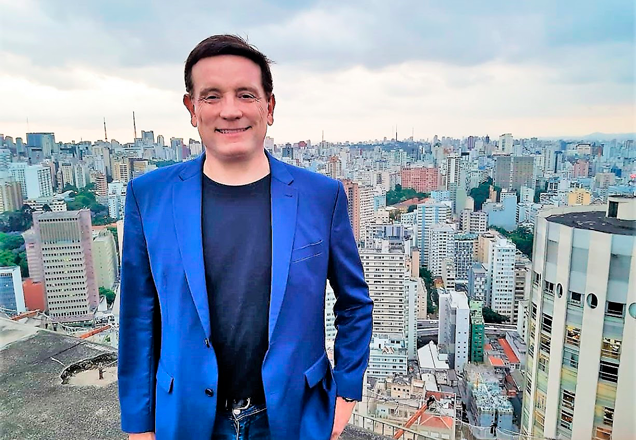 Do alto de São Paulo, com a cidade ao fundo, Roberto Cabrini sorri para a foto