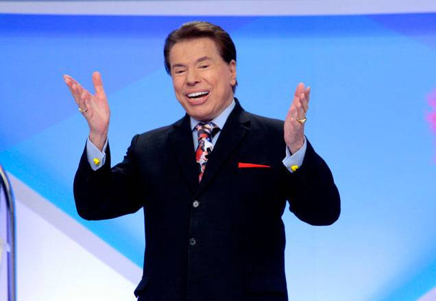 Com terno preto e gravata colorida, Silvio Santos se diverte no palco do programa ao chamar a plateia para participar