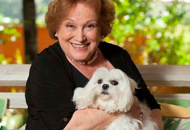 A atriz Nicette Bruno sorri com uma cachorrinha branca nos braços