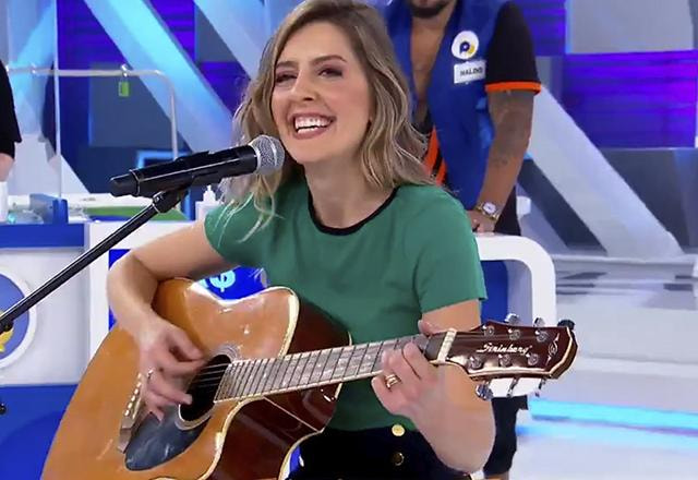 Taisa Pelosi sentada segurando um violão e cantando no microfone | Foto: SBT