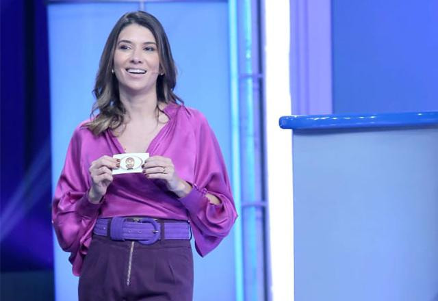 Rebeca está de pé segurando um envelope com as mãos e sorri, ela veste uma roupa toda em tons de lilás | Foto: Lourival Ribeiro