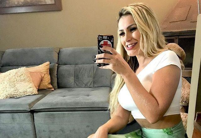 Andressa Urach sorri com o celular na mão