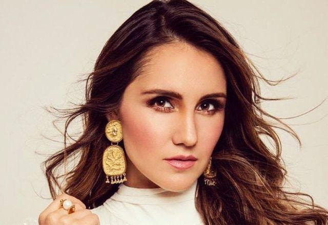 A cantora Dulce Maria em um ensaio fotográico, com blusa creme, sorri