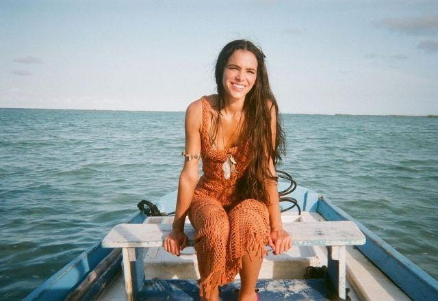 Sentada em um barco, Bruna Marquezine sorri com o mar ao fundo