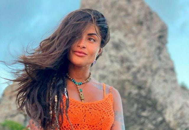 Aline Riscado aparece de blusa laranja colada ao corpo, atrás do Corcovado