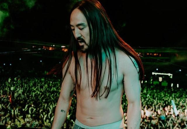 DJ Steve Aoki durante show em um palco com o público ao fundo