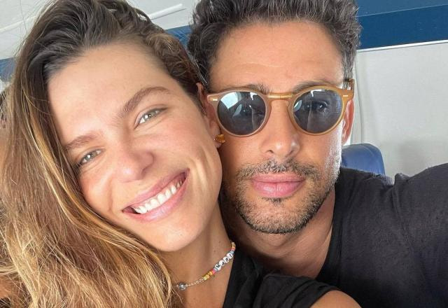 Mariana Goldfarb sorri e Caua Reymond posa ao lado, de óculos. Os dois estão dentro do avião.
