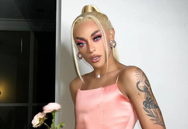 Pabllo Vittar aparece segurando uma flor na mão. Ela está usando um vestido salmão