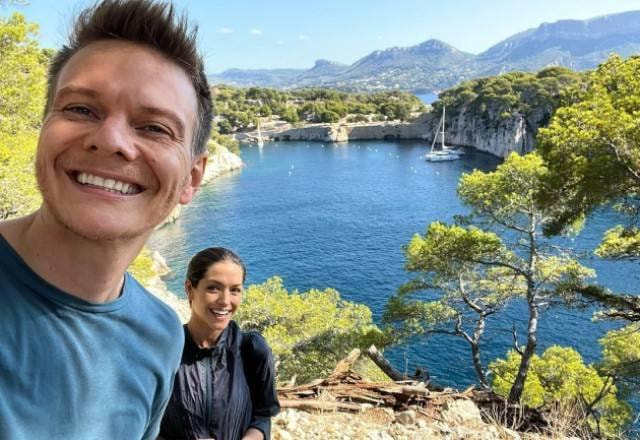 Michel Teló e Thais Fersoza no Sul da França em uma trilha com uma paisagem do mar e de árvores ao fundo