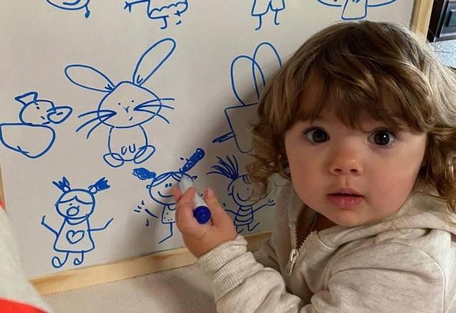 Clara Maria de casaco branco e desenhando em quadro branco