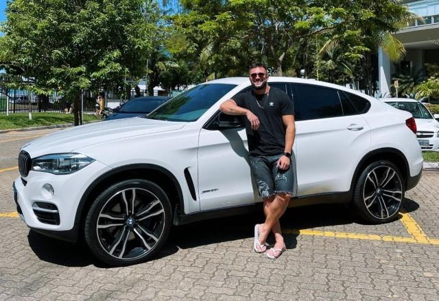 Ex-BBB Arthur Picoli posa sorrindo em frente a uma BMW X4