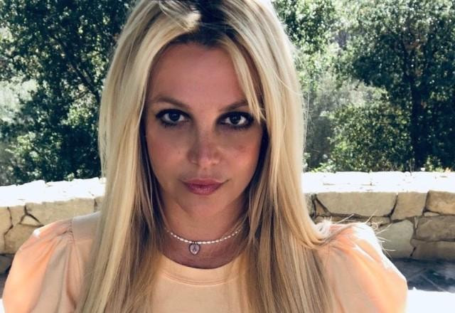 Cantora Britney Spears posa olhando para a câmera com blusa laranja pastel