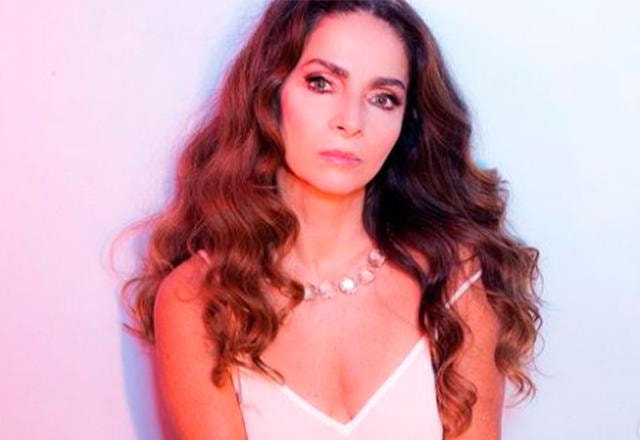 claudia ohana com vestido branco em frente a uma luz colorida