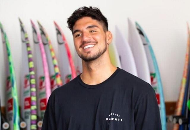 Gabriel Medina posa sorrindo com várias pranchas no fundo