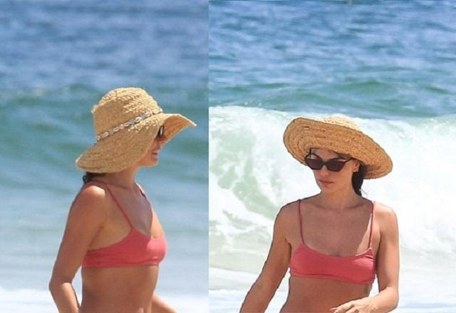 Isis Valverde com biquíni rosa e chapéu de palha desfilando na praia