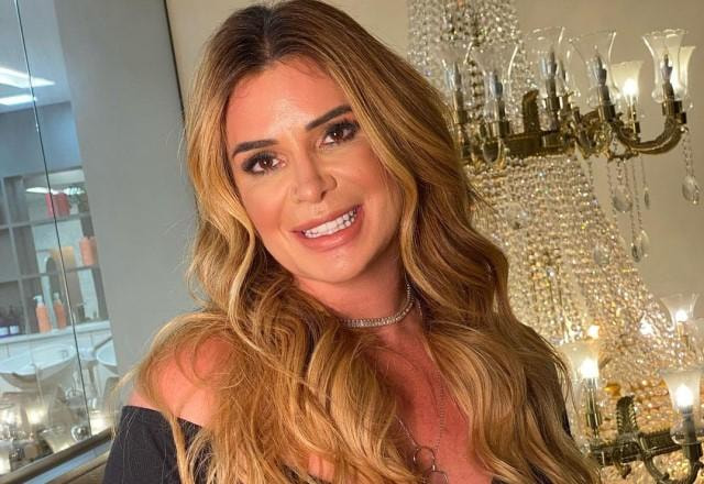 Viviane Tube posa sorrindo em frente a um lustre chique