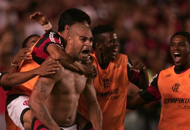 Adriano Imperador sem camisa, flexionando o peitoral e carregando jogadores do Flamengo nas costas