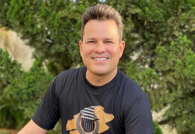 João Neto posa com camisa preta em jardim