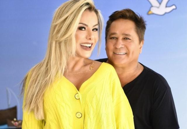 Poliana Rocha posa sorrindo ao lado de Leonardo em fundo azul