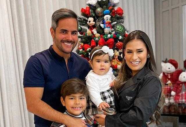 Simone e o marido, Kaká Diniz, posam sorrindo com os filhos, Henry e Zaya. Eles estão na frente de uma árvore de natal