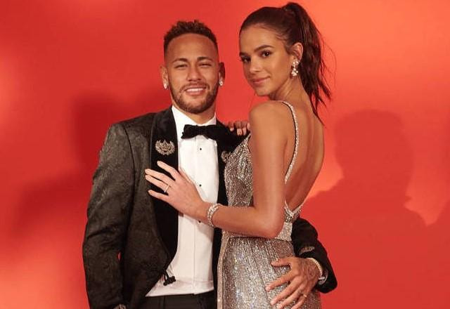 Neymar e Bruna Marquezine posam lado a lado usando roupa de gala e em fundo vermelho