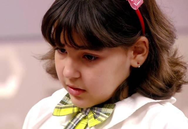 Marcelina de uniforme e com olhar triste