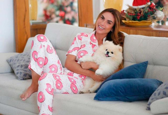 Nicole Bahls no sofá de casa, de pijama e com sua cachorrinha