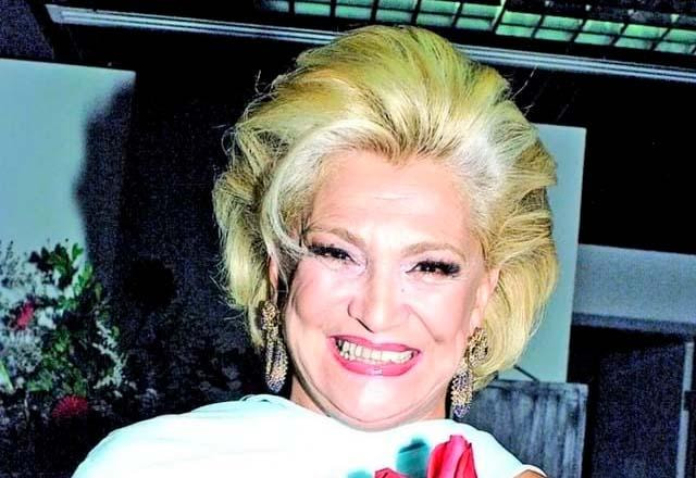 Hebe Camargo sorri enquanto segura ente as mãos um buquê de rosas revermelhas