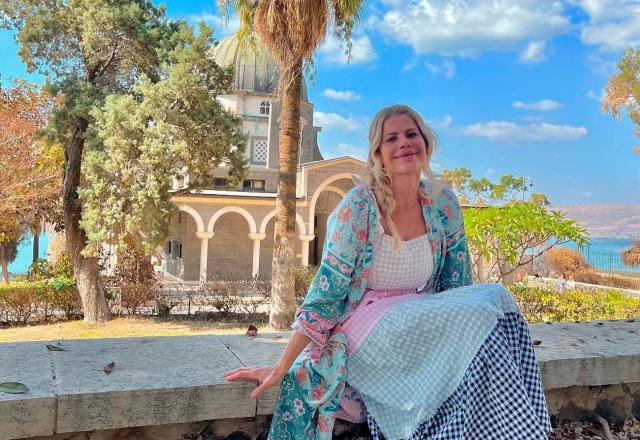A atriz Karina Bacchi posa sentada em sacada com jardim ao fundo