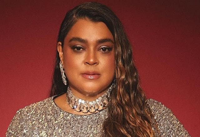 Preta Gil posa com look prata brilhante em fundo vermelho