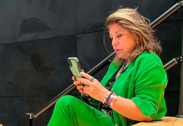 Roberta Miranda está sentada no primeiro degrau de uma escada, olhando para o celular. Ela veste verde