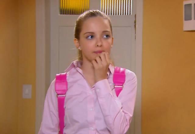 Priscila com expressão tensa e a mão na boca, vestindo uma camisa rosa e com uma mochila rosa nas costas