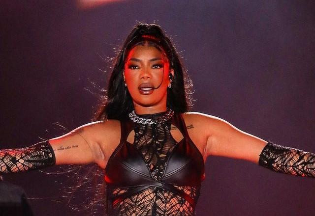 Ludmilla com uma roupa preta, no palco, com os braços abertos e expressão séria
