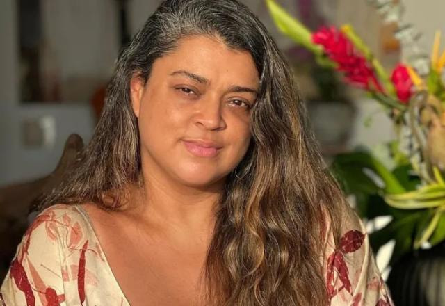 A cantora Preta Gil posa sorrindo em frente a um vaso de plantas