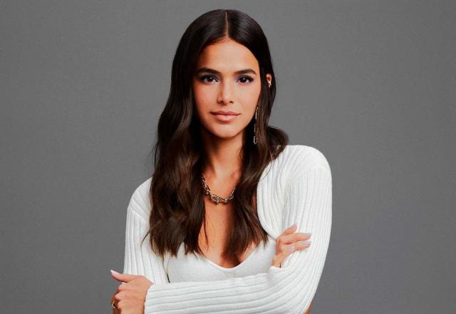 A atriz Bruna Marquezine posa com os braços cruzados e em frente a fundo cinza
