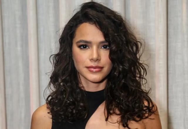 Bruna Marquezine posa olhando fixo para a frente, usando um vestido preto em frente a uma cortina branca