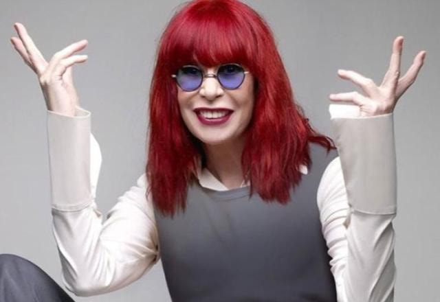 A artista Rita Lee posa sorrindo e com as mãos levantadas