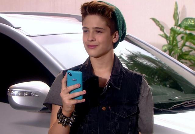 Joaquim segurando um celular azul na mão e com uma expressão de esperteza